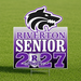 A square graphic design featuring a black and white wolf head mascot outlined in purple above the text 'RIVERTON SENIOR 2027' in purple and white, with a small shield crest reading 'Riverton' at the bottom, on a white background.