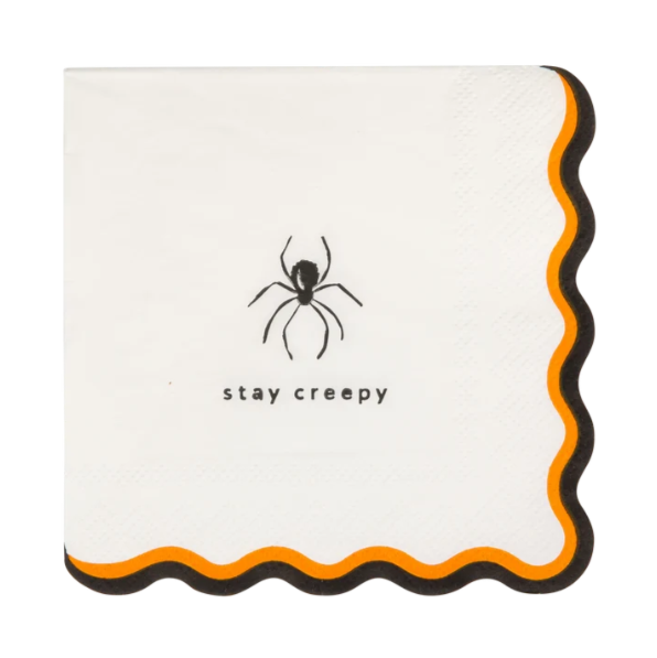 A square white paper napkin with scalloped edges, featuring a black spider graphic and the text 'stay creepy' near the center, with orange and black wavy trim along the border.