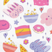A square product shot of a white paper napkin or fabric print featuring a colorful pastel cartoon pattern with bunnies, popcorn bowls, stars, hearts, flowers, and a pink donut.