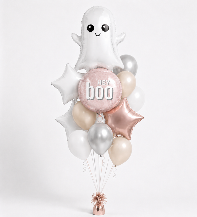 A Halloween-themed balloon bouquet featuring a white ghost balloon, a pink round balloon with 'hey boo' text, star-shaped balloons in white and rose gold, and several metallic silve, champagne and white latex balloons, tied together with a rose gold weight at the bottom.