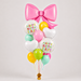 A birthday balloon bouquet featuring a large metallic pink bow at the top, surrounded by assorted round and heart-shaped balloons in pink, white, yellow, mint green, and lime green. Two white round mylar balloons have 'HAPPY BIRTHDAY!' printed on them in colorful letters.