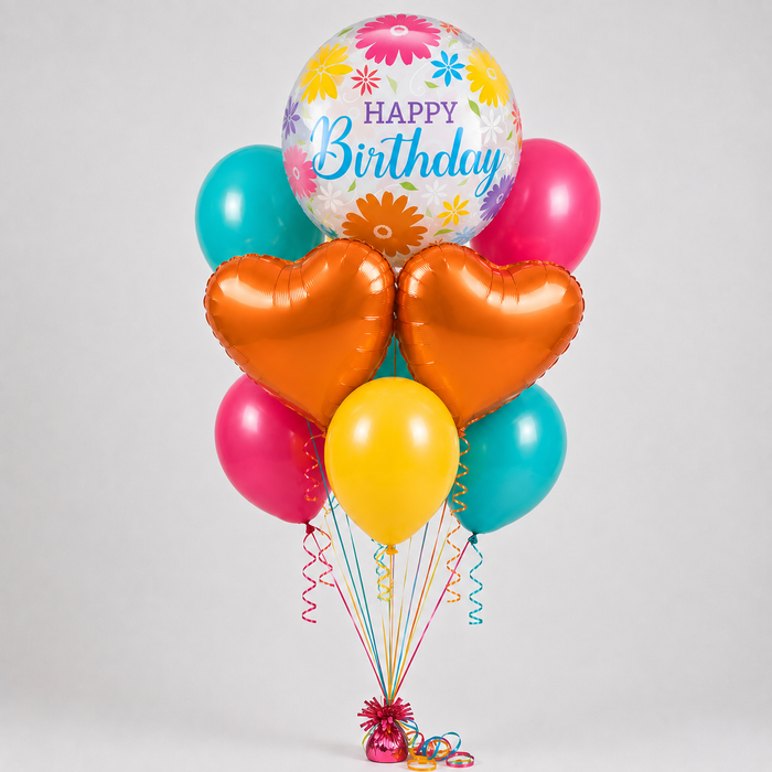 A birthday balloon bouquet featuring a large round balloon with a colorful floral pattern and 'Happy Birthday' text, surrounded by metallic heart-shaped orange balloons, pink, teal, and yellow balloons, tied together with multicolored ribbons and streamers on a light gray background.