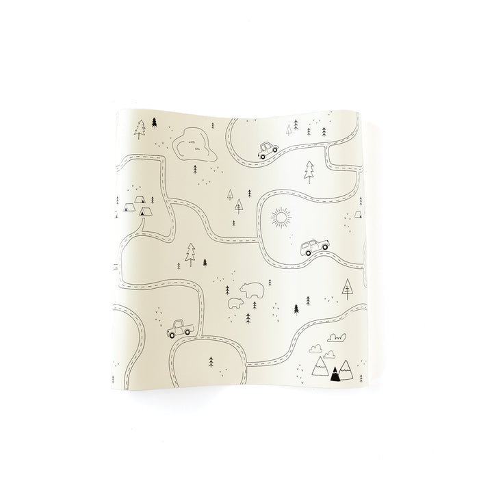 Adventure paper table runner with a cream background and black line-art map design featuring roads, trees, tents, cars, bears, mountains, and outdoor trail details.