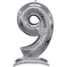 Silver metallic number 9 balloon with a self-standing base, featuring a shiny finish and measurement markings along its curved surface.