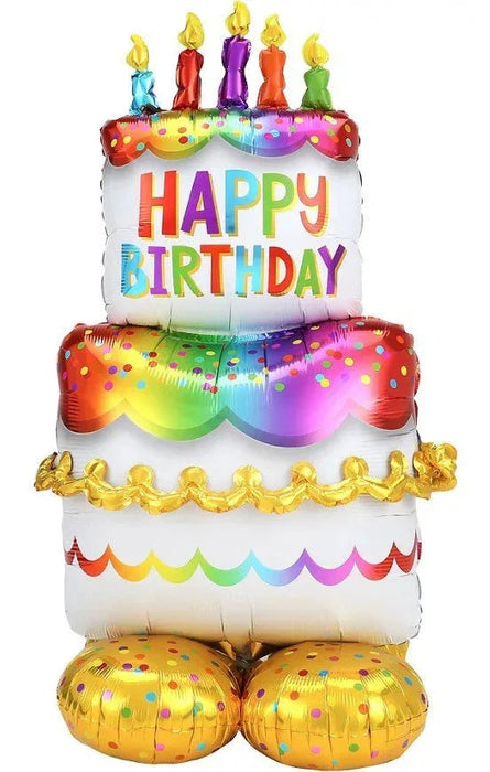 Colorful inflatable birthday cake balloon with five lit candles on top, rainbow polka dots, "Happy Birthday" text in multicolored letters, scalloped garland trim, and gold foil balloon base decorations.