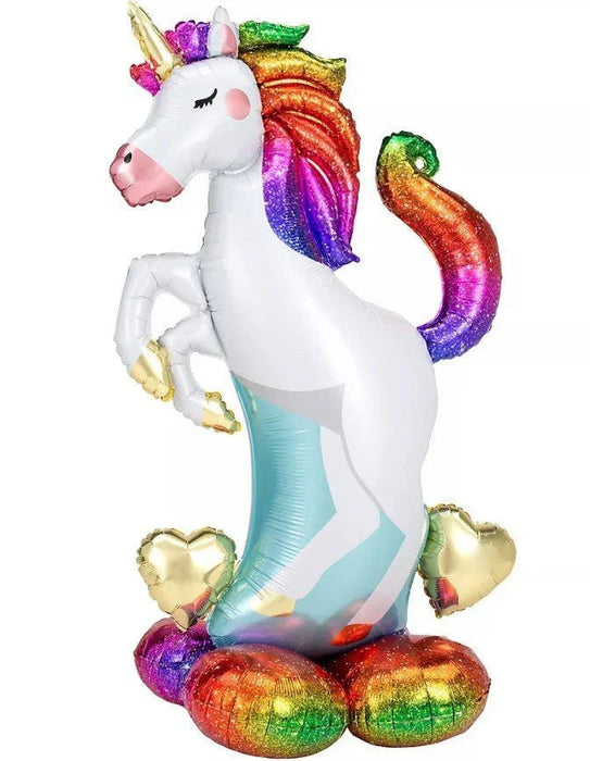 White unicorn-shaped foil balloon with a rainbow gradient mane and tail, gold horn and hooves, pink nose, and turquoise legs, displayed standing upright with colorful heart and egg-shaped balloons at its base.