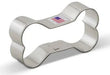 Stainless steel dog bone-shaped cookie cutter with a small American flag label on top, shown at an angle against a white background.