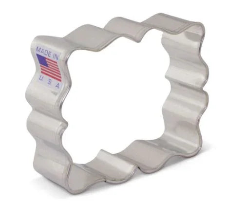 White metal cookie cutter with wavy scalloped edges in a plaque shape, marked "Made in USA" with American flag on the tag.