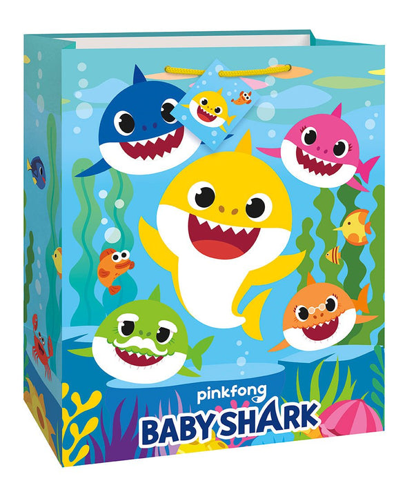 Turquoise gift bag featuring colorful smiling shark characters in blue, yellow, pink, and green with large eyes and open mouths, surrounded by underwater seaweed and small fish on a light blue background.