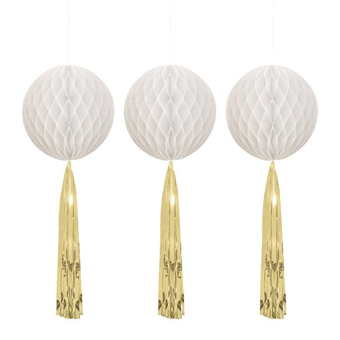 Three white honeycomb ball decorations with gold metallic tassel streamers hanging below each one.