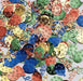 Colorful metallic confetti pieces in red, blue, green, gold, and cream featuring balloon and streamer designs scattered on a white surface.