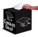Black cubic card box with "Congrats Grad" text and graduation cap illustrations, shown with a hand inserting a white card through the top slot.