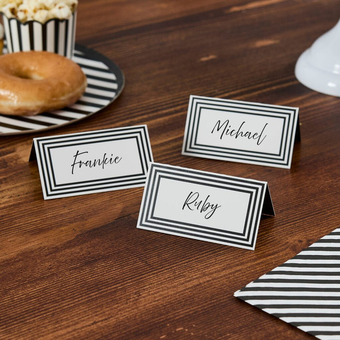 Three black and white striped place cards with handwritten names "Frankie," "Michael," and "Ruby" arranged on a wooden table next to a donut, popcorn, and striped napkin.