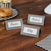 Three black and white striped place cards with handwritten names "Frankie," "Michael," and "Ruby" arranged on a wooden table next to a donut, popcorn, and striped napkin.