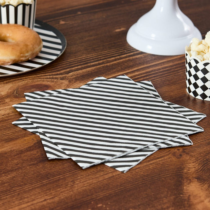Black and white horizontally striped paper napkins displayed in a fan stack on a dark wood table next to a bagel and popcorn container.