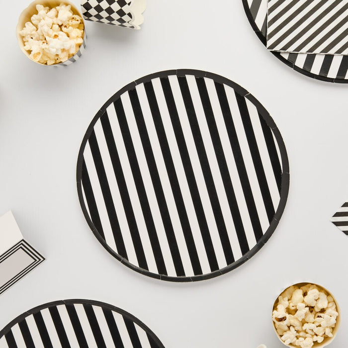 Black and white striped paper plates arranged with popcorn containers on a white background, showing eight circular plates with vertical stripe pattern.