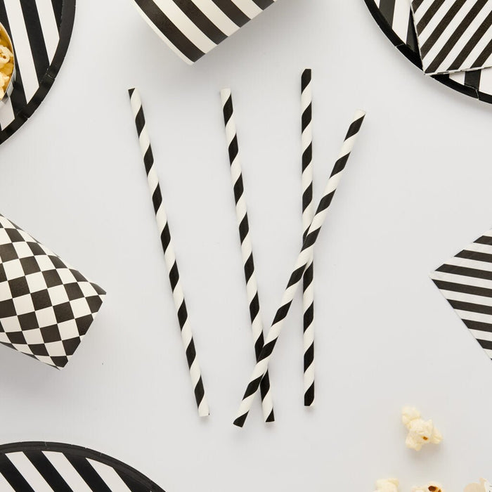 Four black and white spiral twisted paper straws arranged vertically on a white background surrounded by striped and patterned decorative paper elements.