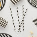 Four black and white spiral twisted paper straws arranged vertically on a white background surrounded by striped and patterned decorative paper elements.