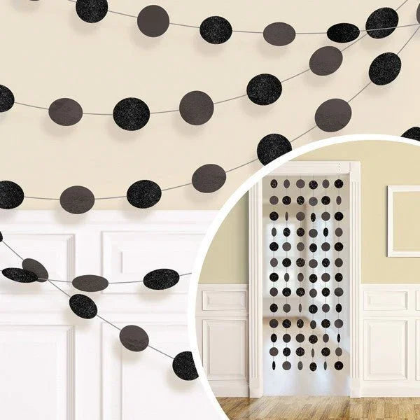 Black and gray glitter circle garland strands draped on a cream wall above white panel doors, showing multiple interconnected strings with alternating textured and matte spheres.