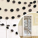 Black and gray glitter circle garland strands draped on a cream wall above white panel doors, showing multiple interconnected strings with alternating textured and matte spheres.