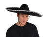 Black sombrero with wide brim trimmed in silver sequined braid and chin strap, displayed on a model wearing a black shirt.