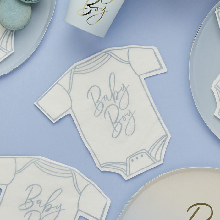 White onesie-shaped napkins with blue trim and "Baby Boy" text arranged on a lavender surface alongside coordinating tableware and decorative items.
