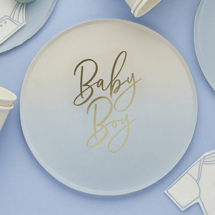 Cream-colored paper plate with "Baby Boy" in gold script lettering, surrounded by coordinating blue ombre plates and white napkins on a lavender background.