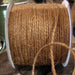 Roll of natural tan burlap jute twine wound on a white spool with a loose strand hanging down.