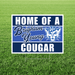 Navy and white yard sign with "HOME OF A Brigham Young COUGAR" text and a cougar mascot logo featuring a BYU hat, displayed on green grass.