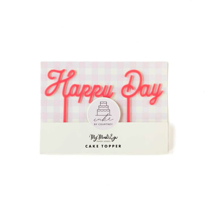 Pink neon "Happy Day" cake topper with a white circular label reading "cake by Courtney" and My Mind's Eye branding on cream packaging.