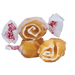 Four golden brown taffy candies with white caramel swirl designs wrapped in white and red paper packaging arranged on a white background.