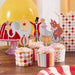 Circus-themed cupcake decorations including four pink-frosted cupcakes with colorful paper wrappers featuring striped, polka dot, and diamond patterns, topped with cardstock picks depicting an elephant, ringmaster, seal, and bear on a unicycle.