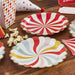 Two scallop-edged paper plates with red and white swirl designs sit on a wooden surface surrounded by popcorn, striped paper straws, and coordinating carnival-themed party decorations.