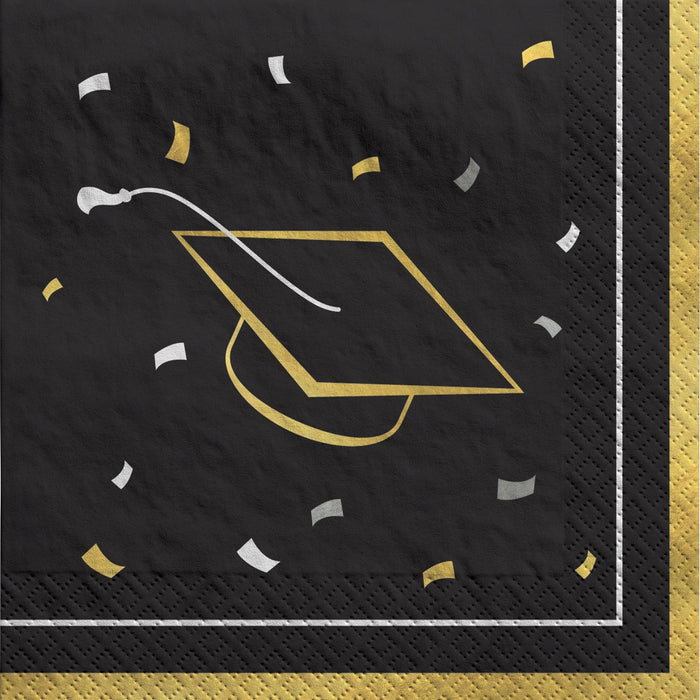 Black beverage napkins with gold and white graduation cap designs and confetti scattered throughout, featuring gold borders on the edges.