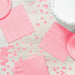 Pink paper napkins and matching plates arranged on a white wood surface with scattered pink confetti circles for party decoration.