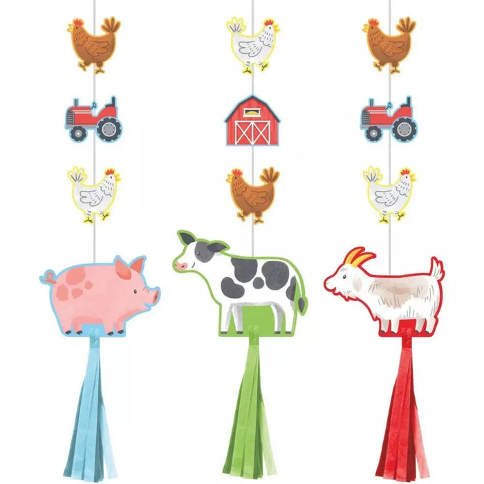Three colorful farm-themed hanging decorations with tassels featuring a pink pig, black and white cow, and white goat, each strung with small farm elements like chickens, tractors, and a barn.