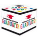 White cubic gift box decorated with colorful "Congratulations Graduate!" text and red mortarboard caps, featuring various academic gown designs on the top panel.