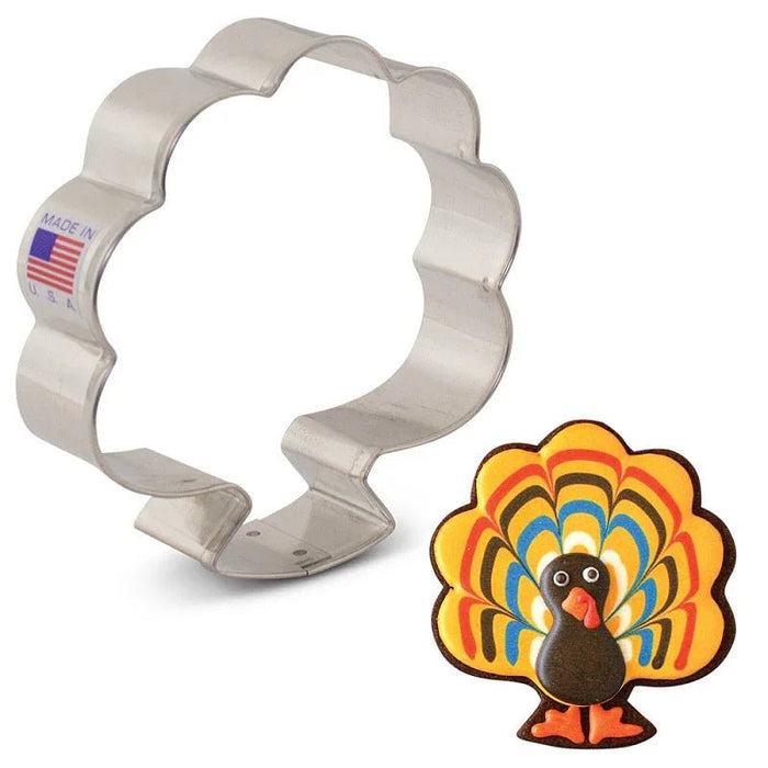 Metal turkey-shaped cookie cutter with wavy edges and "Made in USA" flag label, shown with colorful illustration of a turkey with fanned tail feathers.