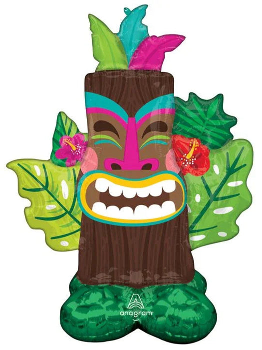 Colorful inflatable tiki mask balloon featuring a brown wooden face with pink and teal stripes, white teeth, tropical feather headdress, and green leaf-shaped wings with pink flowers.