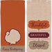 Two Thanksgiving-themed cotton dish towels: one orange with a cream turkey silhouette and "Happy Thanksgiving" text, and one cream with decorative labels reading "Thankful," "Grateful," and "Blessed" in burgundy and brown.