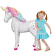 White foil unicorn balloon with pink mane, gold horn, colorful stars on body, and magenta hooves, standing next to a smiling child in a turquoise dress.