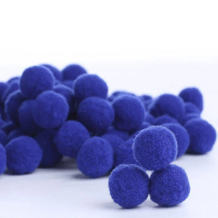 Pile of royal blue fuzzy pompoms scattered on a white surface, with several pompoms in sharp focus in the foreground.