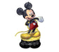 Inflatable foil balloon shaped like Mickey Mouse wearing red shorts and yellow shoes, with black ears and white gloves raised in a waving pose, standing on a black base.