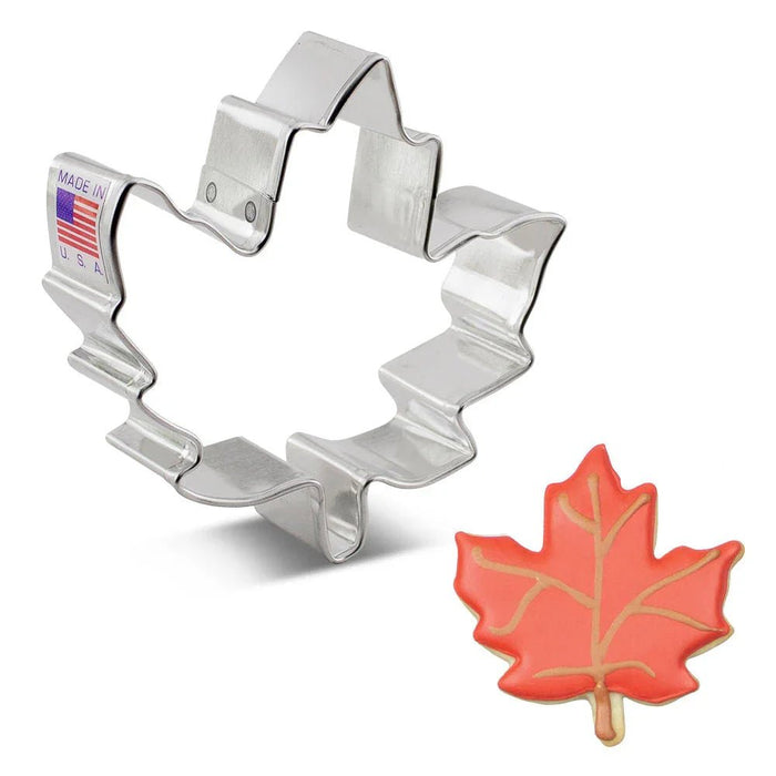 Silver stainless steel maple leaf cookie cutter with "Made in U.S.A." label displayed next to a red decorated maple leaf cookie.