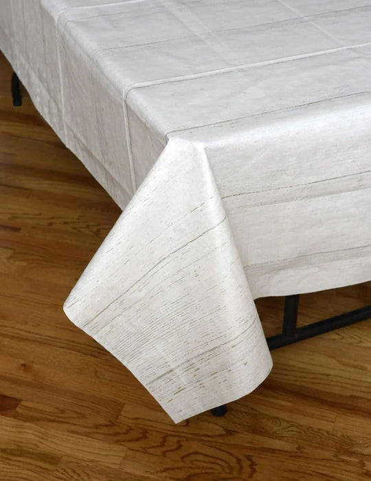White shiplap-patterned tablecloth draped over a rectangular table on a wooden floor, showing the textured wood grain design across the fabric.