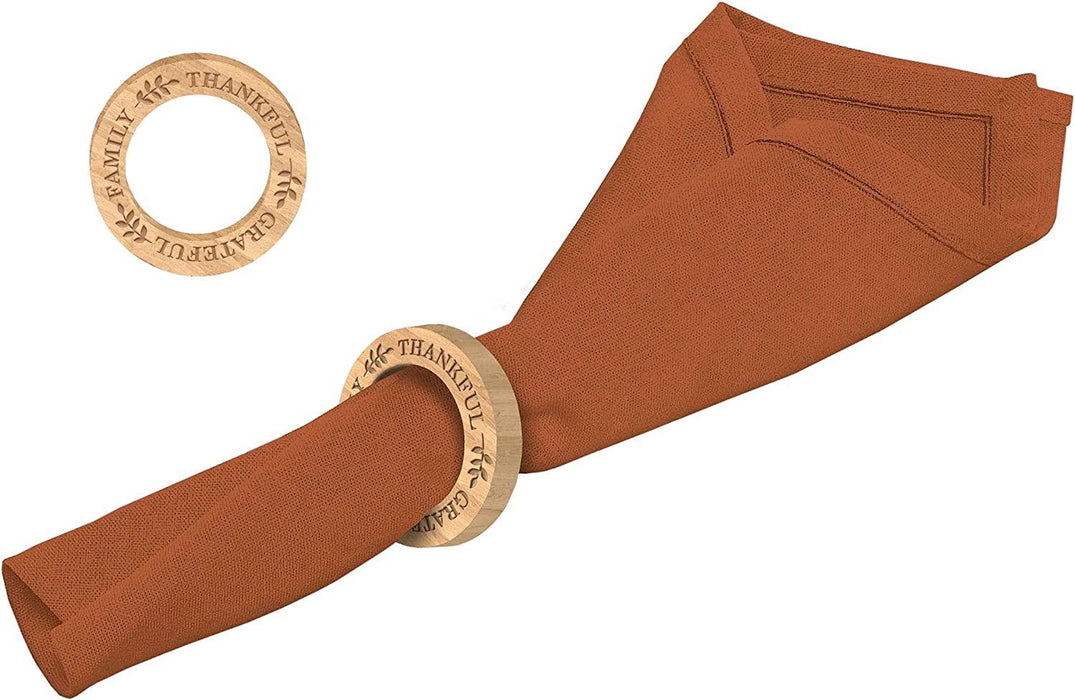 Rust-colored linen napkin rolled through a wooden ring engraved with "Thankful" text, shown with two additional wooden rings displayed separately against a white background.