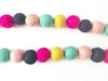 Colorful felt pompom garland string featuring alternating bright pink, dark gray, pale pink, mint green, and yellow fuzzy balls strung together in two horizontal rows.