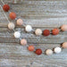Two strands of pompom garland with alternating cream, tan, coral, and rust-colored fuzzy balls on white string displayed on a wooden surface.