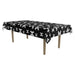 Black rectangular tablecloth with white skull and crossbones pattern, draped over a wooden table with four tan legs.
