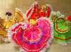 Four handmade corn husk dolls with colorful pleated fabric skirts in yellow, red, pink, and green, decorated with white lace trim and contrasting ribbon accents, displayed on a tan woven background.